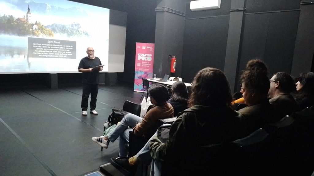 Homem vestido de preto dando aula em auditório do Oswald de Andrade para público.