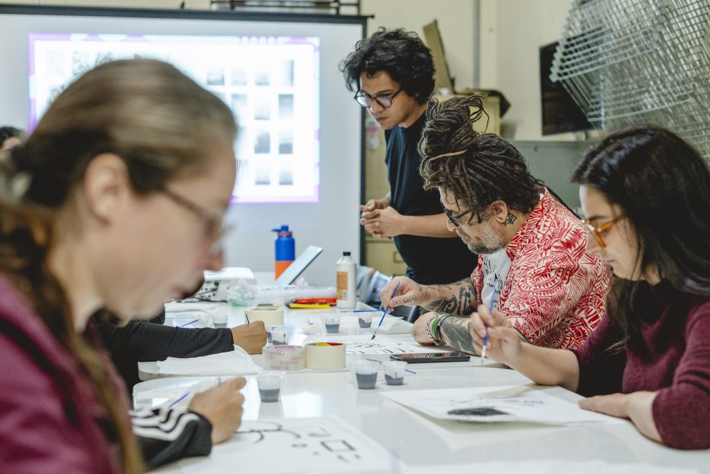 Foto de estudantes e professor em aula prática de desenho em sala de aula.