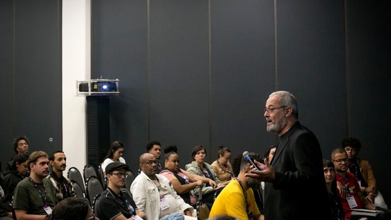 Foto com grupo de pessoas assistindo um homem dando palestra em auditório .