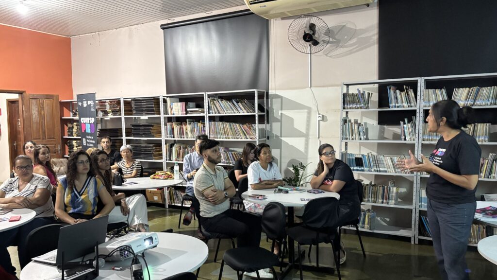 Foto de grupo de pessoas assistindo palestra em biblioteca.